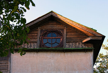 Ancient house with oval window in the attic against blue sky. Vintage house with roof decorated by the carved wooden platbands. Concept of historical buildings of ancient Ukraine