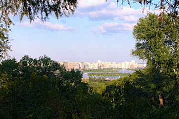 Scenic summer landscape view of Dnipro River and process of construction of high-rise houses on the left bank of Dnipro. Tree leaves border. Hryshko National Botanical Garden. Kyiv, Ukraine