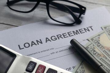 Selective focus of calculator,glasses,pen,dollar note and Loan Agreement letter on a white wooden background.