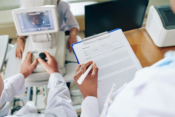 Assistant filling medical history of patient when low vision specialist checking eyesignt of woman