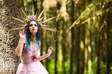 Costume Play.  Sensual Magnificent Crowned Forest Nymph with Flowery Golden Crown Posing in Summer Forest Against High Tree Stem.