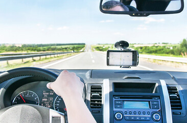 The hand of man is on the steering wheel and gps is on the windshield.