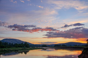 Beautiful golden summer sunrise over the river and mountains. The sun rises over the water surface of the river.