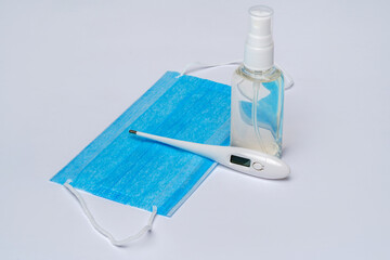 bottle of lotion, sanitizer or liquid soap, electronic thermometer and protective mask over light grey background