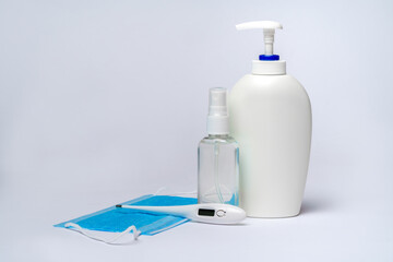 bottle of lotion, sanitizer or liquid soap, electronic thermometer and protective mask over light grey background