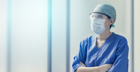 female doctor wearing surgical mask and looking forwards in blurred background with copy space,...