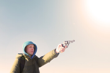 A young man in a hood shoots with a pistol against the sky