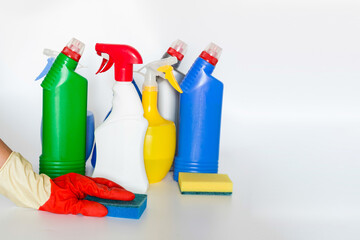 Hand with sponge and Plastic bottles with chemicals for home cleaning