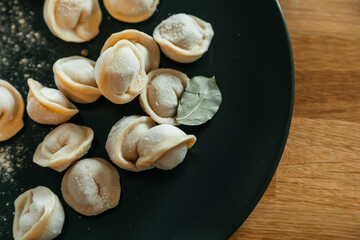 Stuffed homemade dumplings on a dark plate on wooden table. Russian pelmeni.