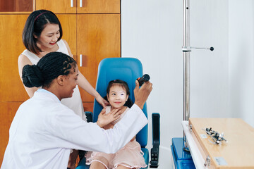 Pediatric ophthalmologist using flashlight when checking eyesight of little smiling girl