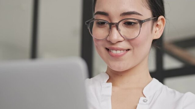 Close up view of Happy elegant pretty asian woman in eyeglasses using laptop computer while sitting on sofa at home