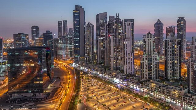 Residential and office complex with many towers aerial dy to night transition timelapse at Business Bay, Dubai, UAE. Bay Avenue Park near big parking lot with cars and traffic on roads