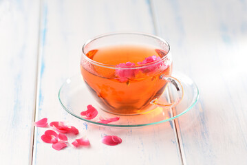 Rose petals tea in a glass cup on the wood table.