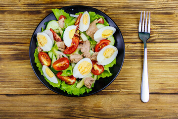 Tasty tuna salad with eggs, lettuce and fresh vegetables on wooden table. Top view