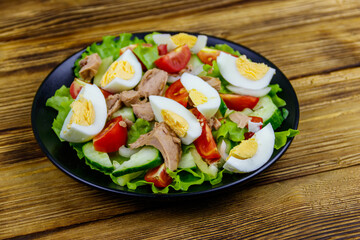 Tasty tuna salad with eggs, lettuce and fresh vegetables on wooden table