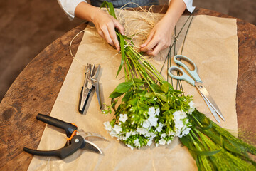 Hände von Floristin beim Blumen binden mit Bast