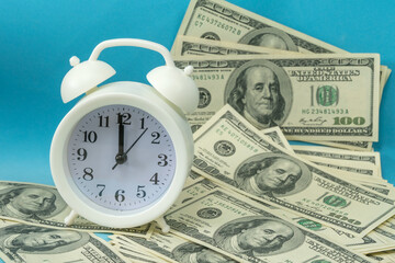 white alarm clock stands on dollar bills on a blue background. Concept of business planning and Finance.