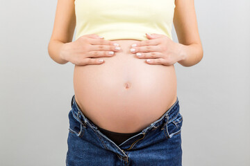 Cropped image of pregnant belly at colorful background with copy space. Expecting mother in opened jeans. Motherhood concept