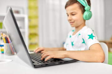 technology, gaming and people concept - boy in headphones playing video game on laptop computer at home