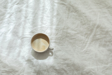 Obraz na płótnie Canvas Cup of fresh coffee on texture of linen cotton rough textile bedclothes. Morning mood. Cappuccino in bed. Empty place, copy space.