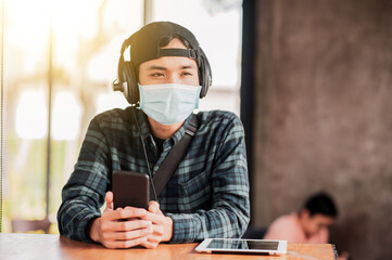 Asian man use mobile phone in cafe indoor a wearing face mask protect corona virus new normal...