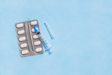 Medical syringe with pills in blister pack on blue background with copy space
