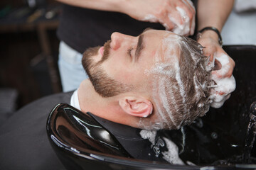 Close up of a bearded man relaxing while barber washes his hair with shampoo