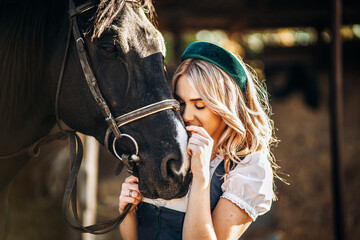 Pretty blonde in traditional dress  take care of big black horse at the farm