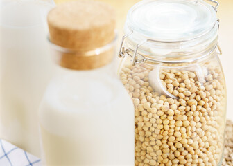 Two glass bottles of fresh and homemade soy milk with glass jar full of organic soybeans on wooden table. Alternative healthy milk, lactose intolerance drink, vegan and plant based diet concept. 