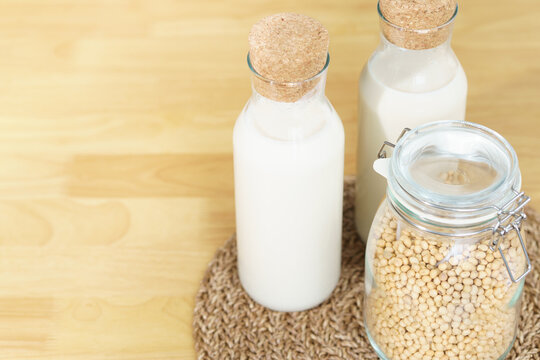 Two glass bottles of fresh and homemade soy milk with glass jar full of organic soybeans on wooden table. Alternative healthy milk, lactose intolerance drink, vegan and plant based diet concept. 