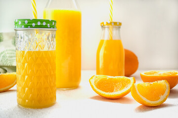 Glass bottles with orange juice stand on a white surface against a black wall. Nearby lie two slices of sweet juicy orange. The concept of a healthy diet, detox diet, drinking diet. Close-up
