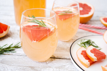 Summer refreshing drink with grapefruit and rosemary in transparent glasses stands on a white tray on a light wooden table. Nearby are striped cocktail tubes. Detox diet, vitamins.