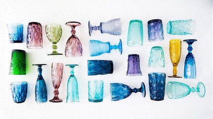 Multi-colored glass empty wine glasses and glasses lie on a white background. Beautiful vintage tableware made of multi-colored glass: blue, green, yellow, pink, purple.