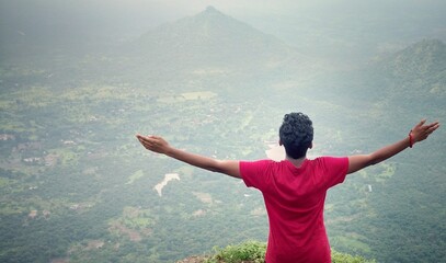 Young person standing  with raising his hands  in front of mountain for relaxing, freedom and wellness, enjoying natural view