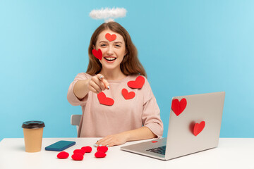 Hey you! Joyful angelic woman with kind expression sitting at workplace, all covered with sticker...