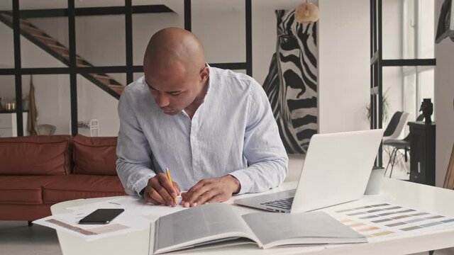 A handsome african american man is working with paper documents sitting at table at home