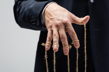 partial view of puppeteer in suit with strings on fingers isolated on grey