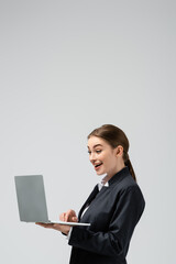happy young businesswoman using laptop isolated on grey