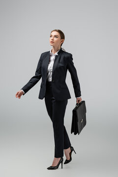 Young Businesswoman Walking With Leather Suitcase Isolated On Grey