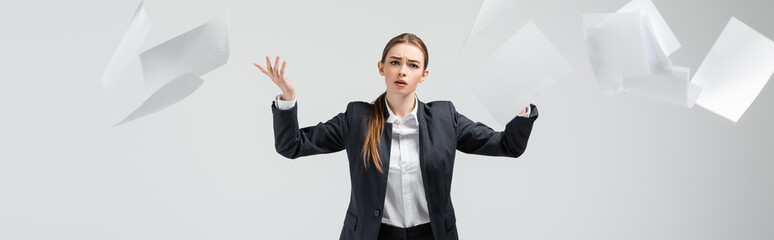 displeased businesswoman in suit throwing papers in air isolated on grey, panoramic shot