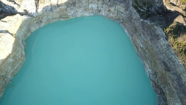 A smooth, top down drone capture of a turquoise blue Kelimutu lake in Flores, Indonesia. The lake is located in volcano crater and surrounded by steep slopes. Golden hour. Natural phenomenon
