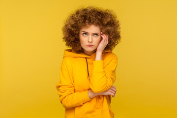 Hmm, need to think! Portrait of confused pensive curly-haired woman in urban style hoodie having...
