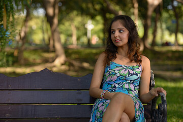 Young beautiful Indian woman thinking and sitting at the park outdoors