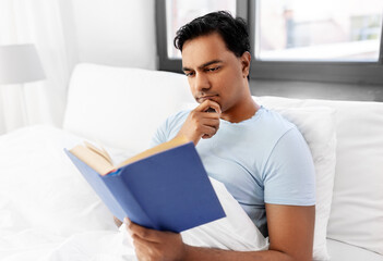 Obraz premium people, bedtime and rest concept - indian man reading book in bed at home