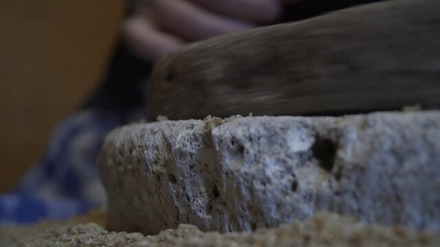The ancient quern stone hand mill with grain. The woman grinds the grain into flour with the help of a millstone. Men's hands rotates a millstone. Old grinding stones turned by human hands