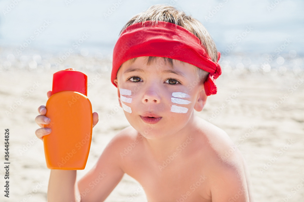 Wall mural Sunscreen (suntan lotion) is on hipster boy face before tanning during summer holiday on beach. Child (kid) is holding container of sunscreen (not far from Trieste, Italy).