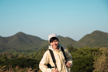 Fototapeta na wymiar Smiling Asian young man in Long-sleeved shirt and grey hat hiking standing at mountain peak above clouds Hiker outdoor. Maetip Reservoir Lamphun Province, Northern Thailand Province in the morning.