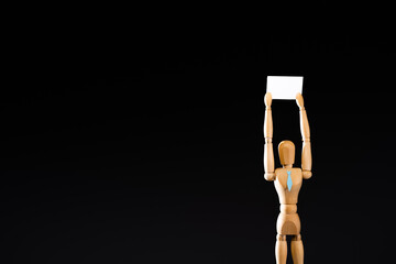 wooden marionette in tie holding blank placard isolated on black