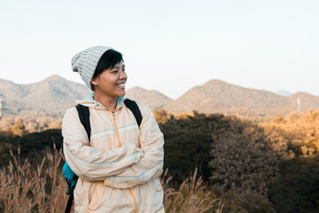 Smiling Asian young man in Long-sleeved shirt and grey hat hiking standing at mountain peak above clouds  Hiker outdoor. Maetip Reservoir Lamphun Province, Northern Thailand Province in the morning.