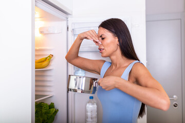 Bad Food In Fridge, young woman in holding her nose because of bad smell from food in refrigerator at home